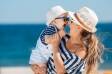 Mama i beba na plaži nose šešire i sunčane naočale za zaštitu od sunca